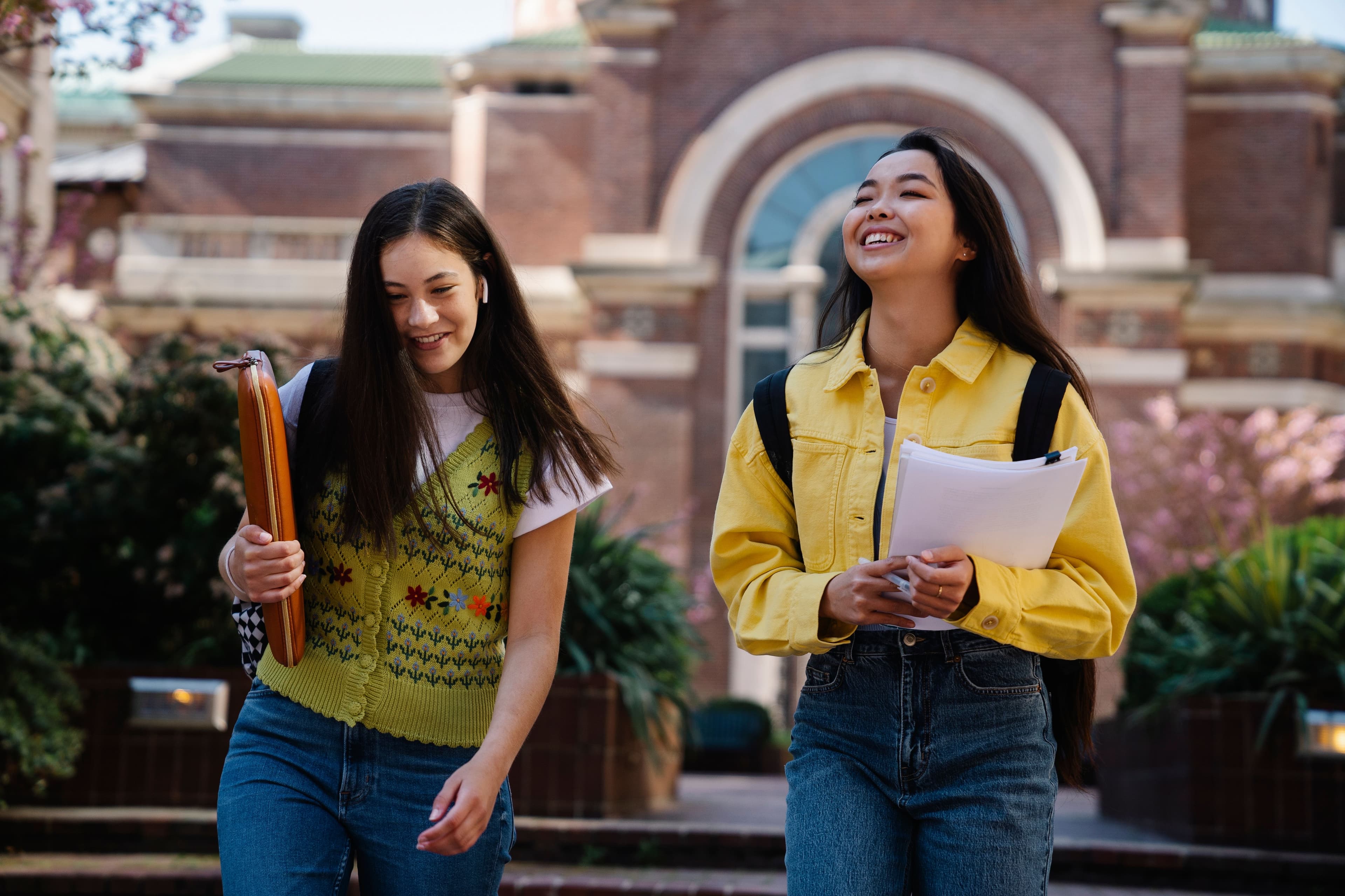 Two students carrying notebooks outside a campus building